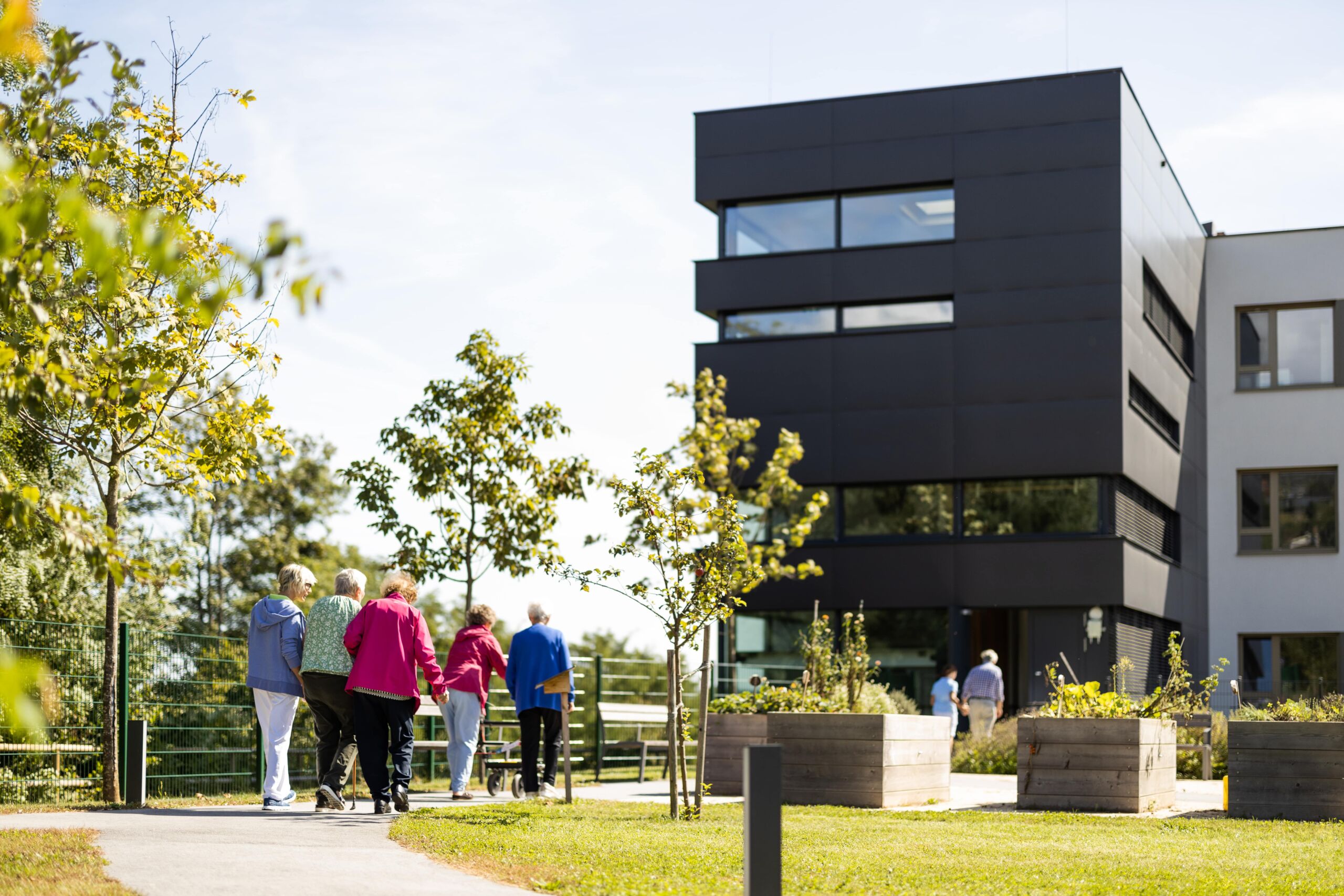 Bewohner:innen des Seniorenhaus Menda im Gespräch im Gartenbereich, sonniger Sommertag