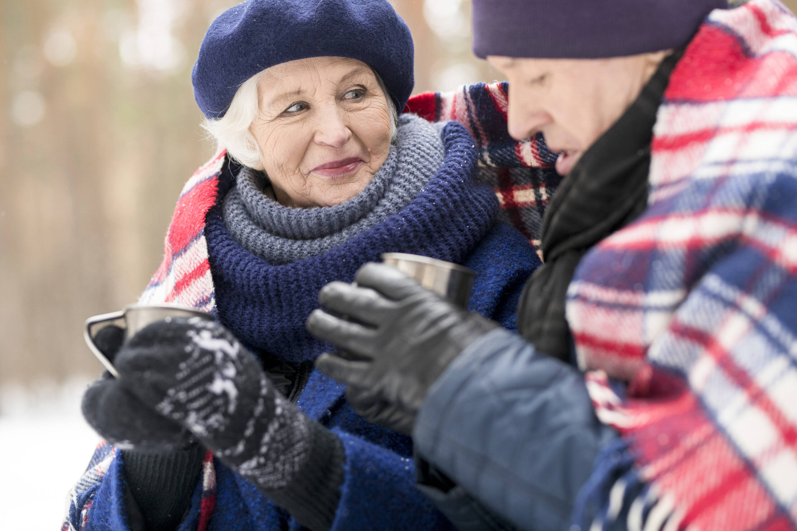 Zwei Senioren sind warm angezogen im Winter draußen und trinken Tee