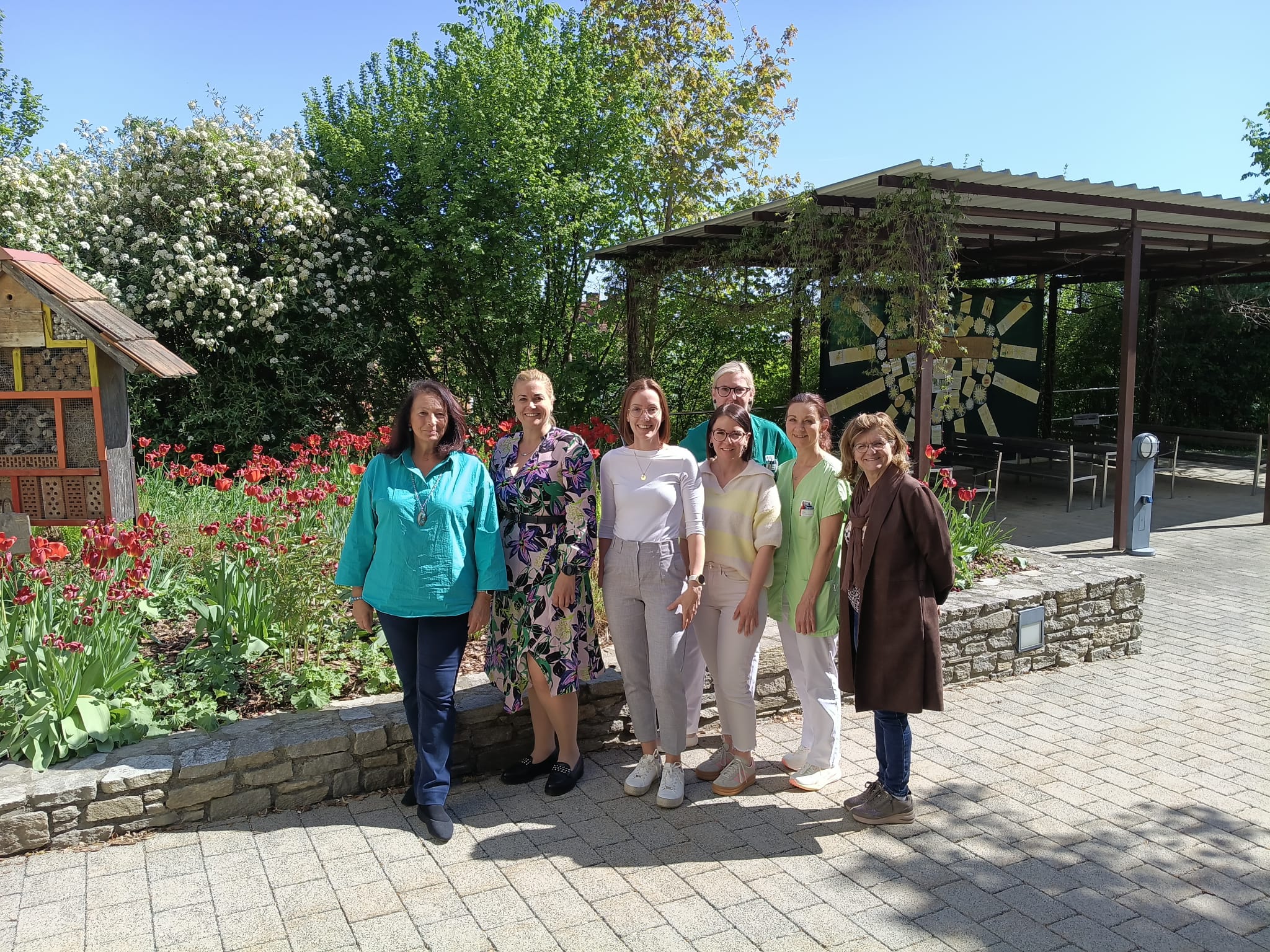 Mitarbeiterinnen des Seniorenhaus Menda im Garten – Teamfoto vor blühenden Blumen und Sitzbereich