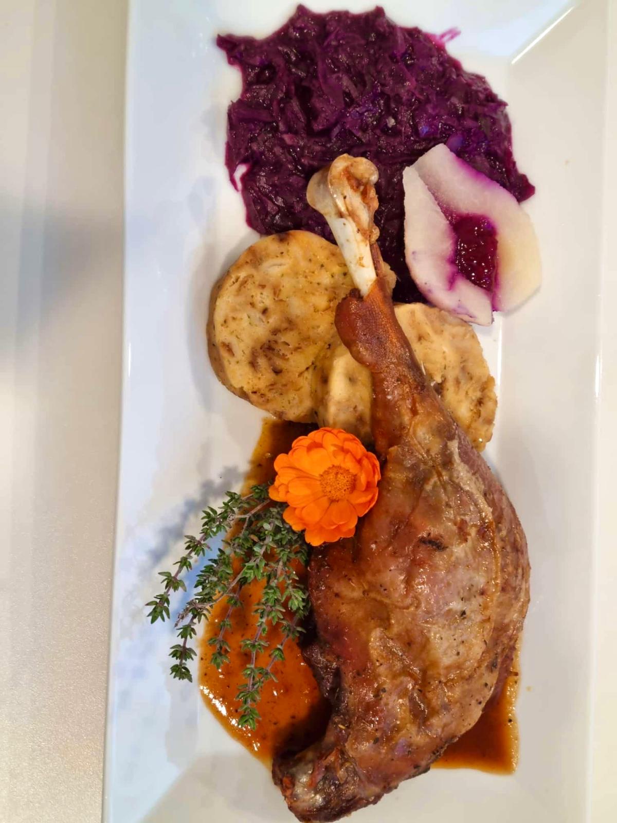 Entenkeule mit Knödel, Rotkraut und Preiselbeer-Garnitur aus der Vogelperspektive auf rechteckigem weißen Teller fotografiert.