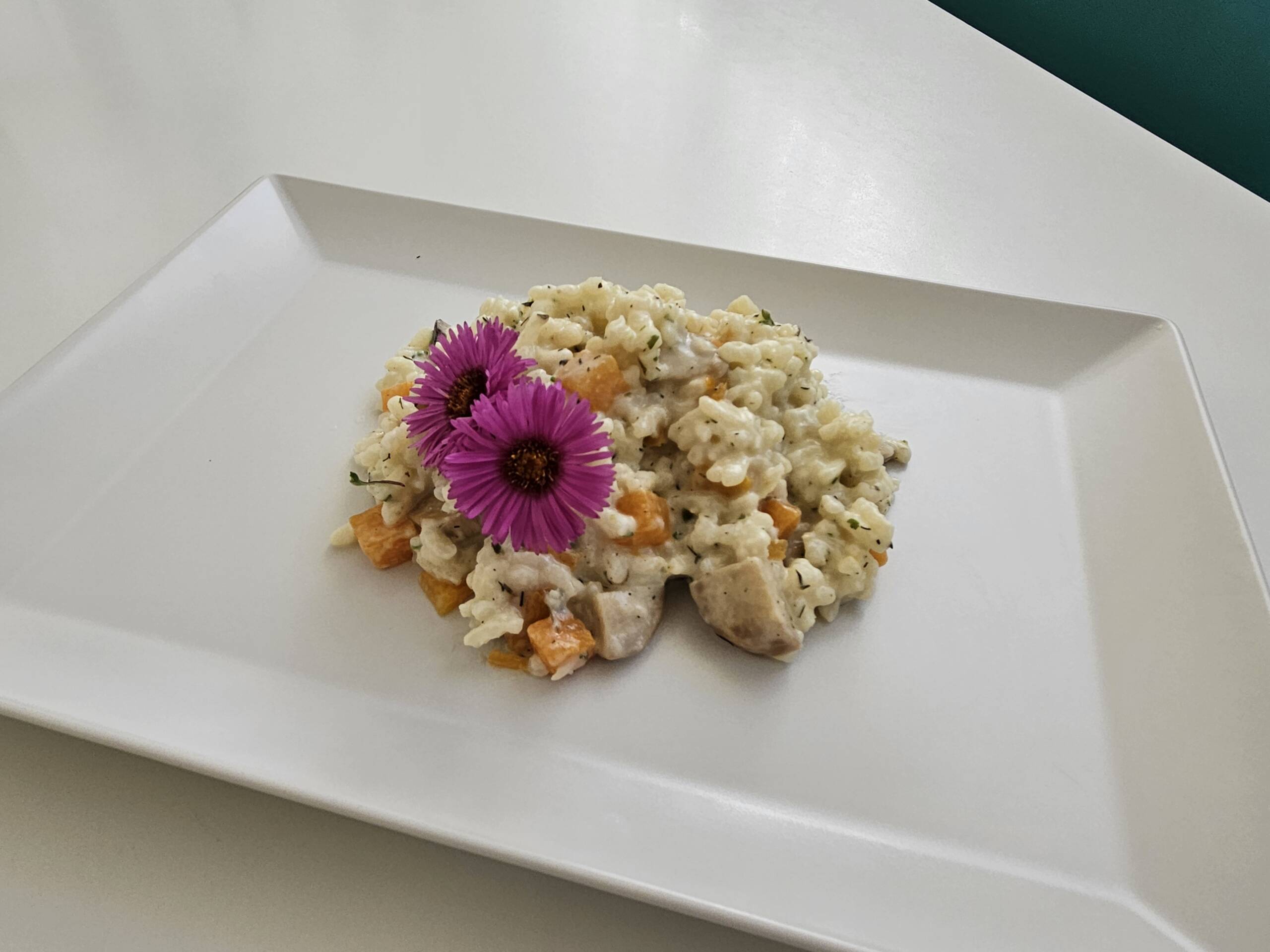 Herbstlich genießen: Saisonale Menüs bei Menda 6 Herbstrisotto mit Kürbiswürfeln, Pilzen und lila essbaren Blüten auf eckigem weißen Teller