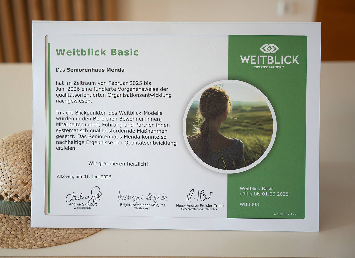 „Gold Standard“: Seniorenhaus Menda erhält das Weitblick-Zertifikat 7 Das Zertifikat „Weitblick Basic“ steht auf einem Tisch neben einem Strohhut mit Sonnenblumen. Es ist gültig bis 1. Juni 2028.